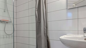 Een badkamer met witte betegelde wanden, een douche met glazen deur en een witte wastafel.