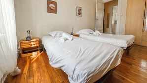 Een hotelkamer met twee bedden, houten vloeren, een nachtkastje met een lamp en een deur die naar een andere kamer leidt.