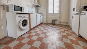 Een keuken met een wasmachine, een magnetron en een raam met uitzicht op gebouwen.