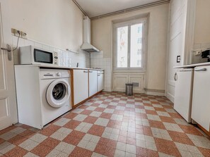 A kitchen with a washing machine, a microwave, and a window with a view of buildings.