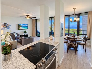 A modern kitchen with an island, a dining area with a view, and a living room with a TV and artwork.