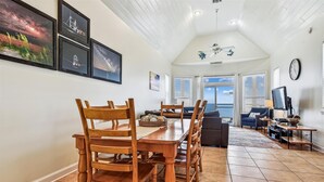 A dining area with a wooden table and chairs, a sofa, and a television. There are framed pictures on the wall and a ceiling fan. - Welcome to The Sandbox! (St. George Island)