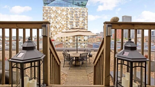 A wooden deck with a table and chairs, overlooking a cityscape with modern buildings. - Huge Penthouse - Birmingham Central - Balcony (Birmingham)