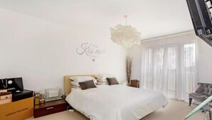 A modern bedroom with a large bed, a Louis Vuitton and Chanel bag on the nightstand, a chandelier, and a 'Kiss me' wall decoration. - Huge Penthouse - Birmingham Central - Balcony (Birmingham)