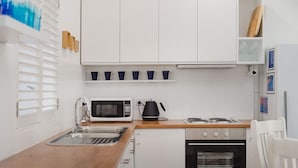 Une cuisine compacte avec des meubles blancs, un four à micro-ondes, une bouilloire et une cuisinière.