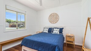 Une chambre avec un grand lit, deux tables de chevet, un banc en bois, une fenêtre donnant sur un beau paysage et un élément décoratif mural.