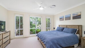 Quarto com cama, ventilador de teto e grandes janelas.