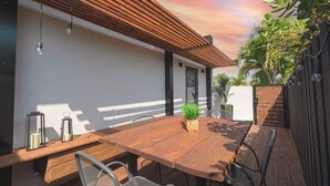 Un espace de restauration en plein air avec une table et des chaises en bois, entouré d’un mur blanc et d’une clôture en bois.