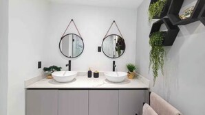 Une salle de bain moderne avec deux miroirs ronds, un plan de toilette blanc et une décoration murale géométrique noire.