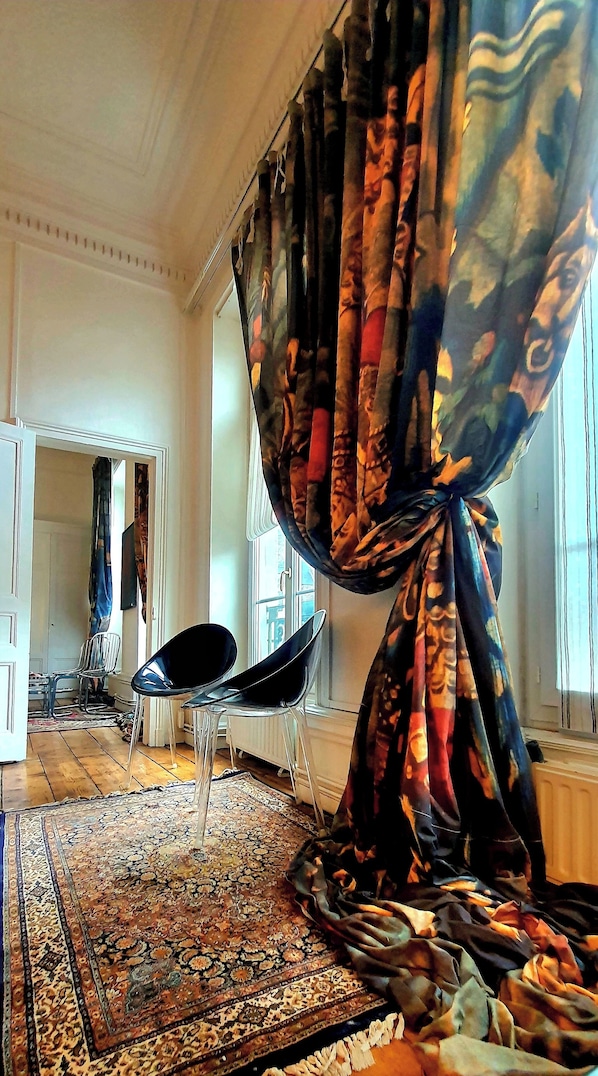 A room with a patterned rug, a chair, and a curtain tied in a knot.