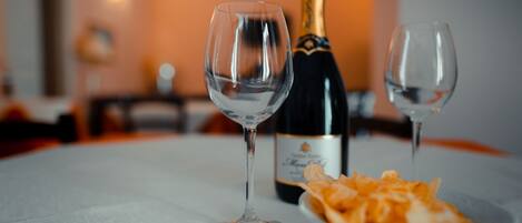 Una mesa con dos copas de vino vacías, una botella de champán y un bol de aperitivos.