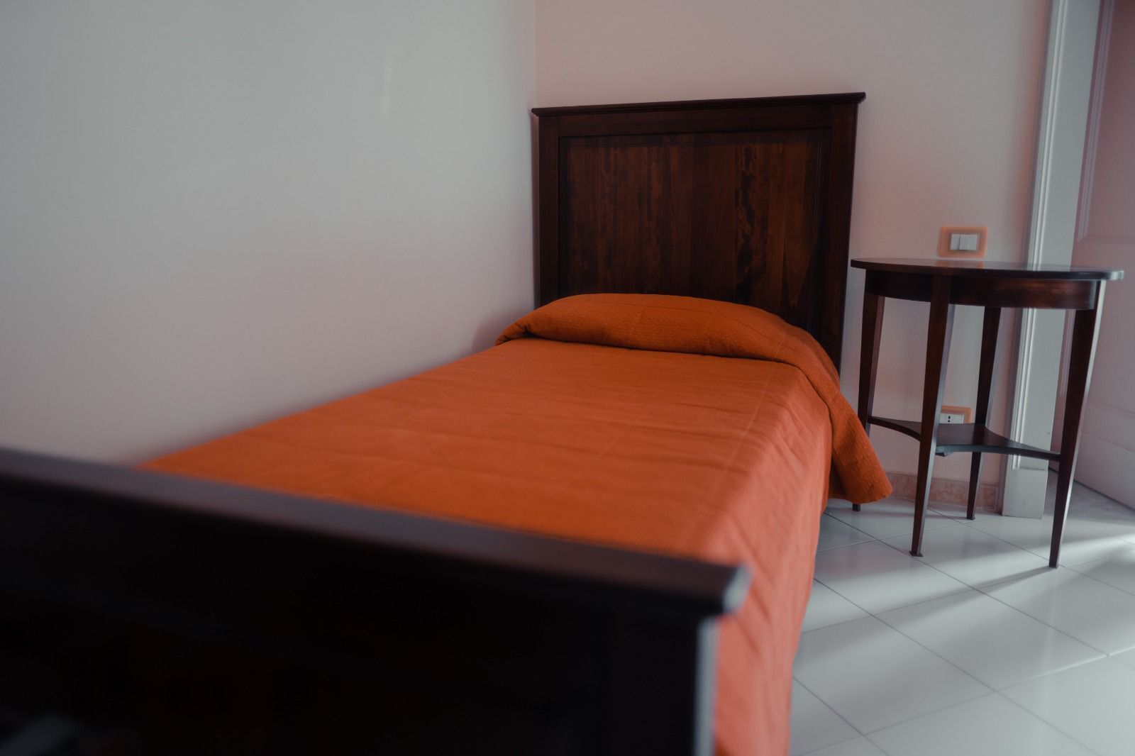 Une chambre à coucher avec un lit, une tête de lit en bois, une petite table et un sol carrelé de carreaux blancs.