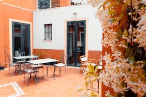 Un patio esterno con tavoli e sedie, una parete bianca e una porta.