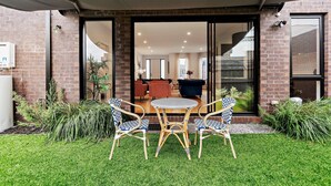 A patio with a table and chairs, a brick wall, and a glass door leading to an interior space with furniture. - Capel Luxe (Capel Sound)