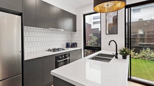 A modern kitchen with grey cabinets, a white countertop, a built-in oven, and a large window offering a view of the outside. - Capel Luxe (Capel Sound)