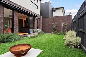 A modern house with a well-maintained lawn, a patio with chairs, and a rustic fire pit.