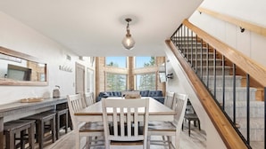 A dining area with a wooden table and chairs, a chandelier, and a staircase with wooden railings.
