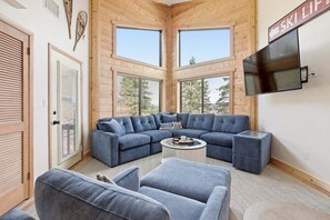 A modern interior with a sectional sofa, a flat-screen TV, and large windows. - Seven Springs 1 BR Loft Condo by RedAwning (Champion)