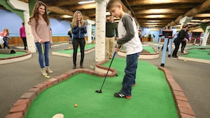 Een indoor midgetgolfbaan met spelers en een putting green.