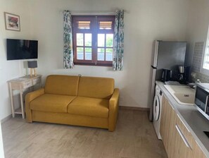 Ein kompakter Wohnbereich mit Sofa, Fernseher, Waschmaschine und Küchenzeile.