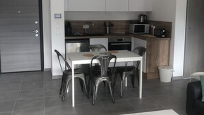 Una cocina moderna con armarios blancos, un microondas y un hervidor. Hay una mesa de comedor con cuatro sillas y una pequeña alfombra en el suelo.