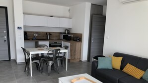 Una sala moderna con un sofá negro, una mesa de centro blanca y un comedor con una mesa y sillas blancas.