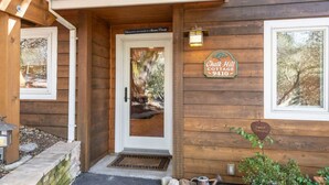 A wooden cottage entrance with a door, a sign reading "Chalet Hill Cottage 9410", and a small garden area with a potted plant. - Vineyard Cottage w/ Fire Pit | Chalk Hill Wine Country (Healdsburg)