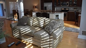 A living room with a sofa, remote controls, and a dining area with chairs and a table.