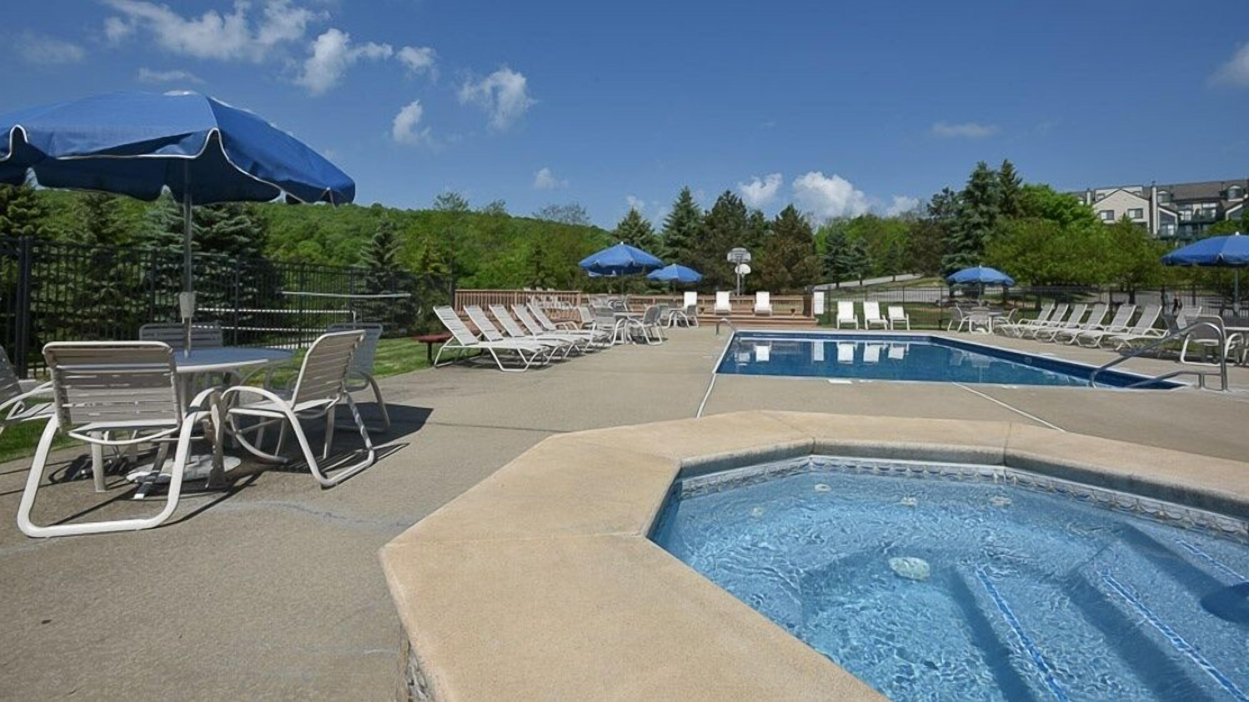 A pool area with lounge chairs and umbrellas, surrounded by greenery and buildings.