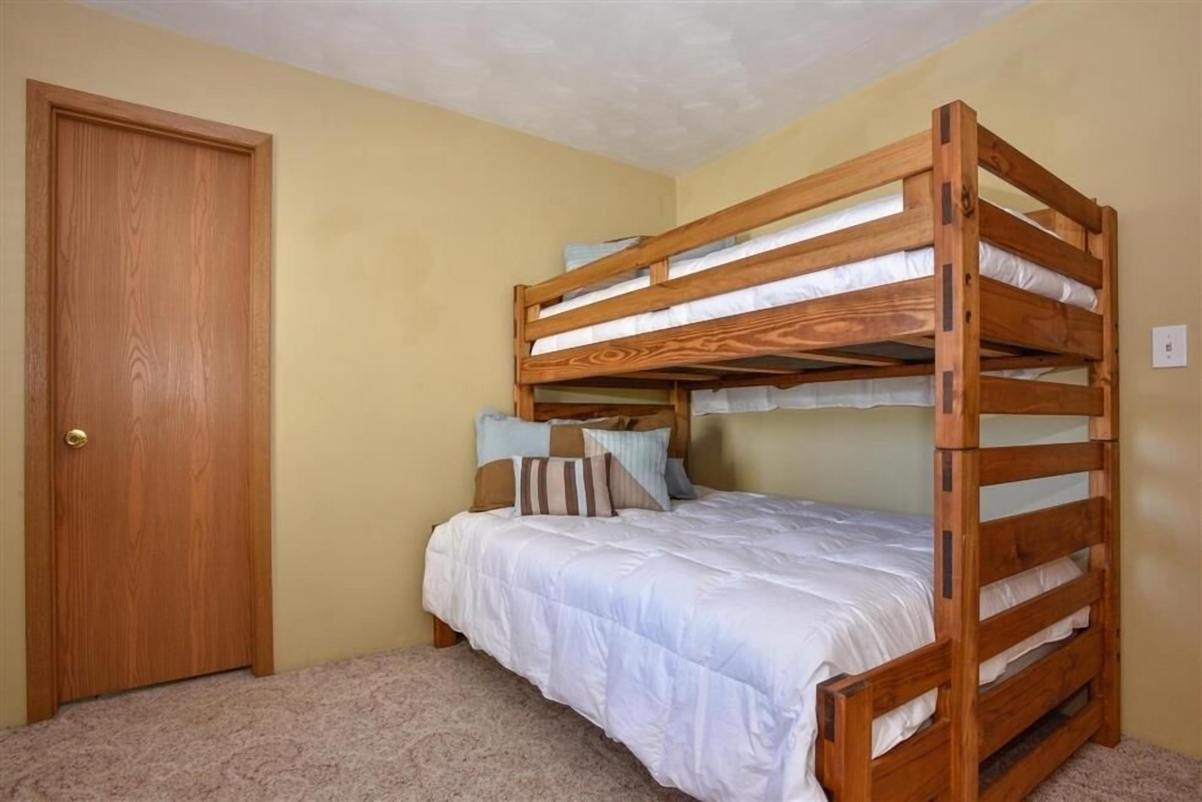 A bunk bed with white bedding and multiple pillows, a wooden door, and beige walls.