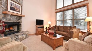 A cozy living room with a stone fireplace, a television, a wooden coffee table, and a comfortable couch. - Seven Springs 4 BR Premium Condo, Sleeps 9 by RedAwning (Champion)