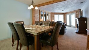 Un coin repas avec une table et des chaises en bois, un lustre et une vue sur l’extérieur grâce à de grandes fenêtres.