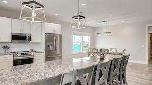 A modern kitchen with granite countertops, stainless steel appliances, and a dining area with wooden chairs. - Soggy Pollards 5 Bedroom Home by RedAwning (Rockport)