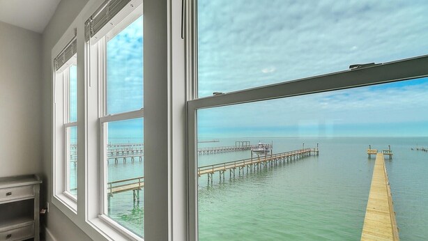 A room with large windows overlooking a calm sea and a wooden pier. - Soggy Pollards 5 Bedroom Home by RedAwning (Rockport)