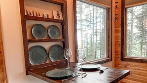 A wooden dining table with plates and cutlery, a wine glass, and a shelf with decorative plates.