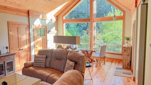 A cozy living room with a large window, wooden ceiling, and a sofa.