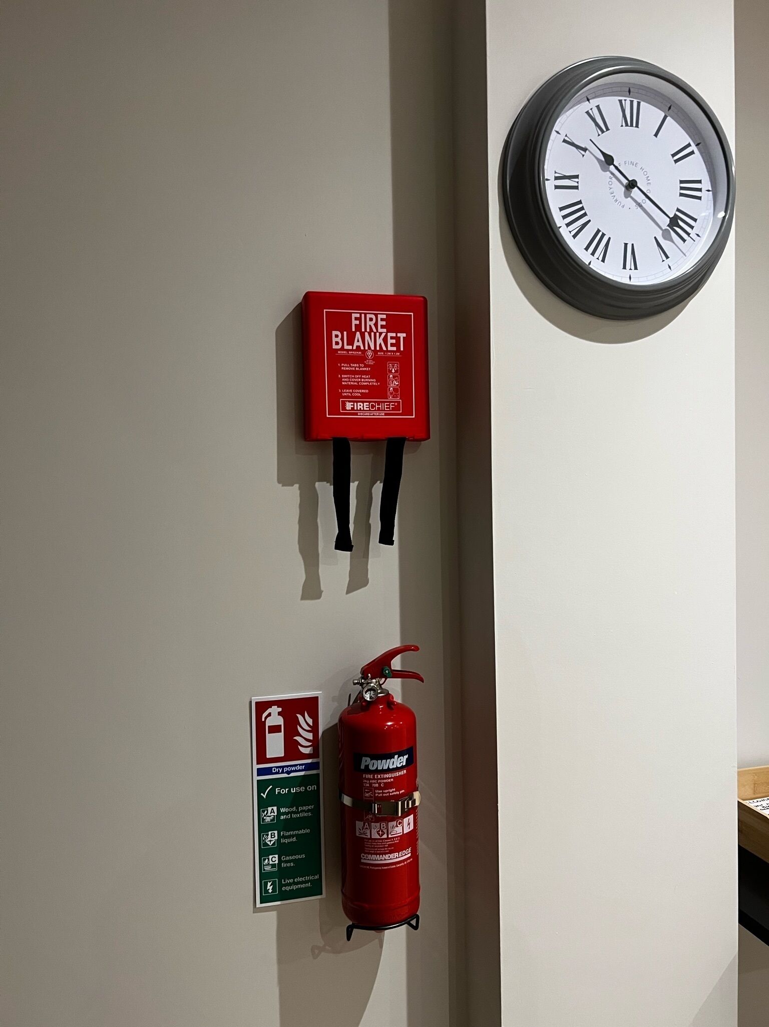 A wall-mounted clock, a fire blanket, and a fire extinguisher.