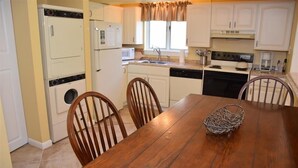 A compact kitchen with a wooden dining table, chairs, a washing machine, a microwave, and a stove.
