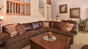 Un salon avec un canapé marron à motifs, une table basse en bois et un escalier doté d’une rampe en bois.
