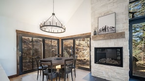 A dining area with a large table and chairs, a stone fireplace, and a view of the outdoors through large glass doors. - Winterleaf 4 Bedroom Home by RedAwning (Telluride)