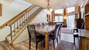 A spacious living area with a wooden staircase, a dining table with chairs, and a large window providing natural light. - Seven Springs Stoneridge 3 BR Loft Standard Condo, Pet Friendly! by RedAwning (Champion)