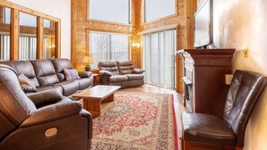 Ein gemütliches Wohnzimmer mit Ledersofas und Kamin, großen Fenstern und einem Fernseher.