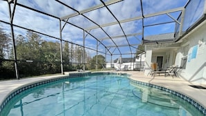 En pool med klart vatten och ett säkerhetsstaket runt om, omgiven av ett hus och träd.