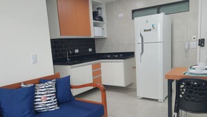A compact kitchenette with a refrigerator, stove, and microwave. There is a small dining table with chairs and a sofa with cushions. - PRAIA FLATS TEMPORADA BLUE 03 NO CENTRO DE PORTO DE GALINHAS (Ipojuca)