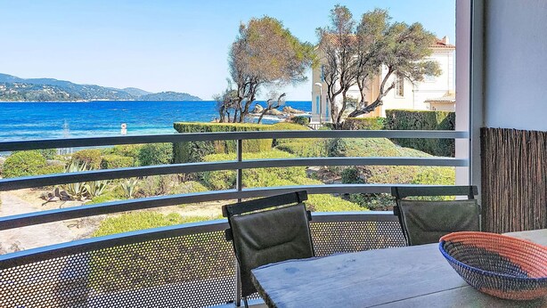 Varanda com vista para o mar, uma mesa, cadeiras e uma cesta de palha.