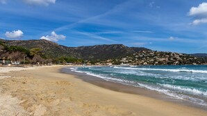Uma praia com montanhas ao fundo, céu claro e mar calmo.
