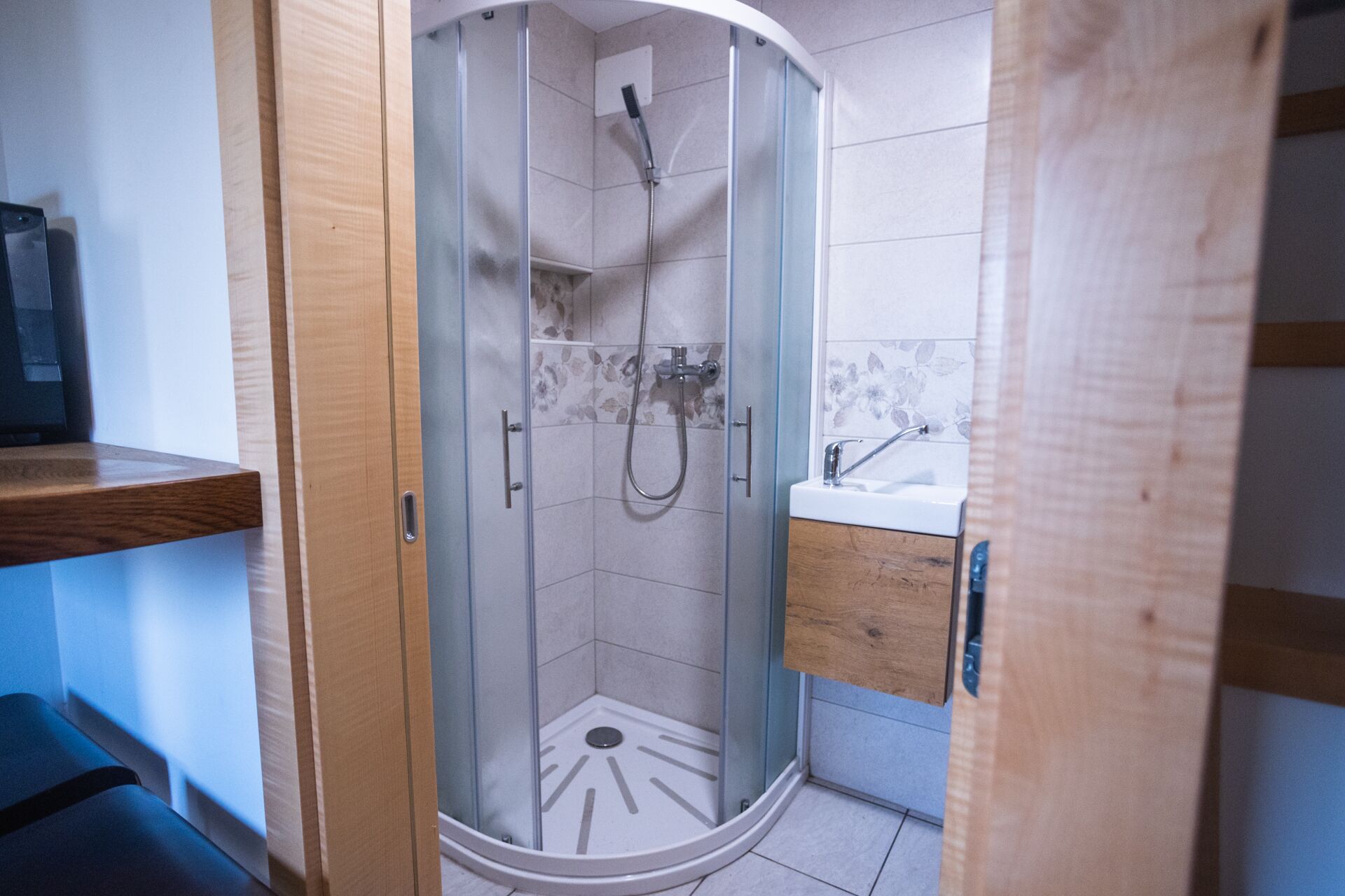 Un baño moderno con cabina de ducha acristalada, tocador de madera y lavamanos blanco.