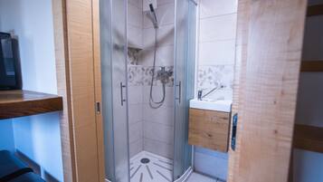 Un baño moderno con cabina de ducha acristalada, tocador de madera y lavamanos blanco.