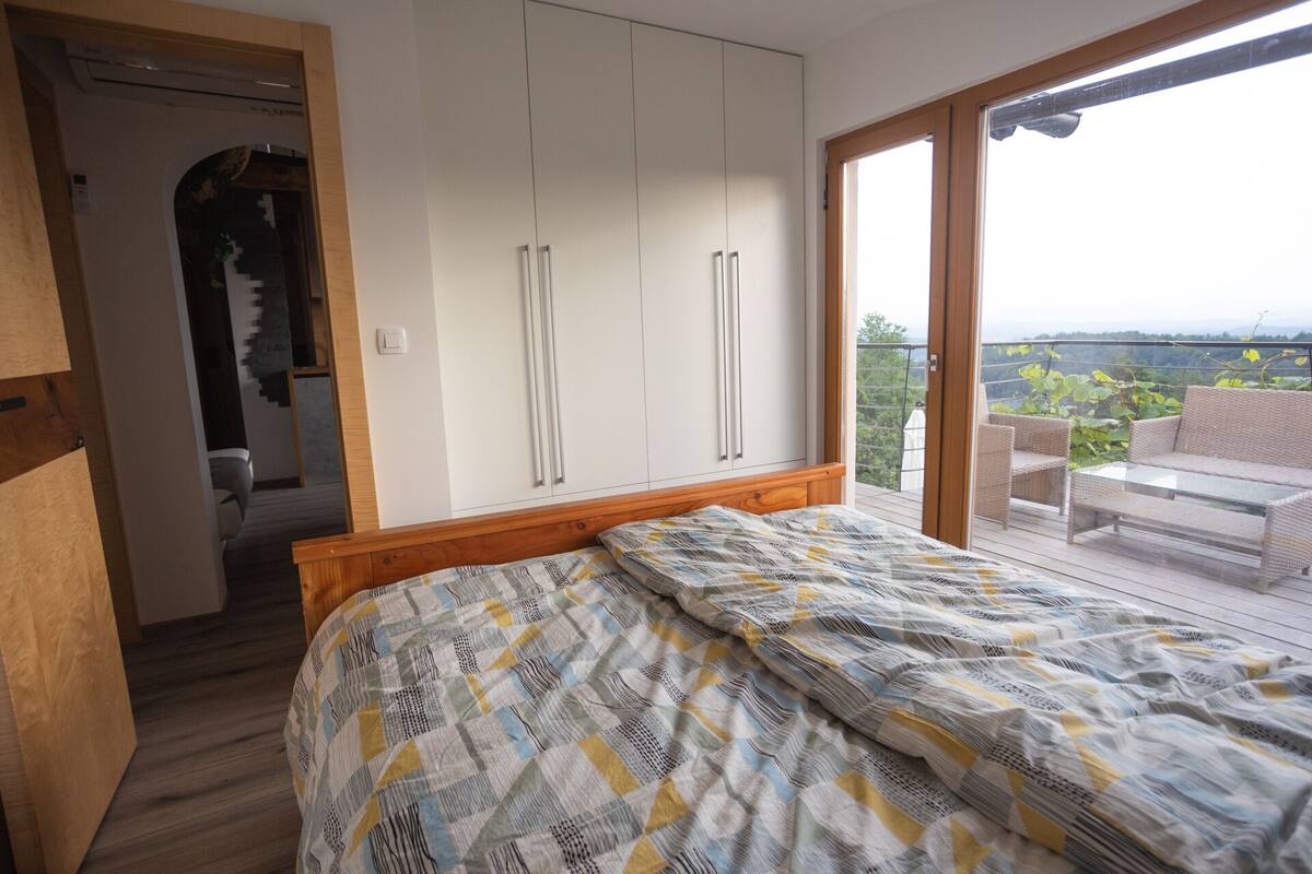 A bedroom with a bed, a wardrobe, and a balcony with outdoor furniture.