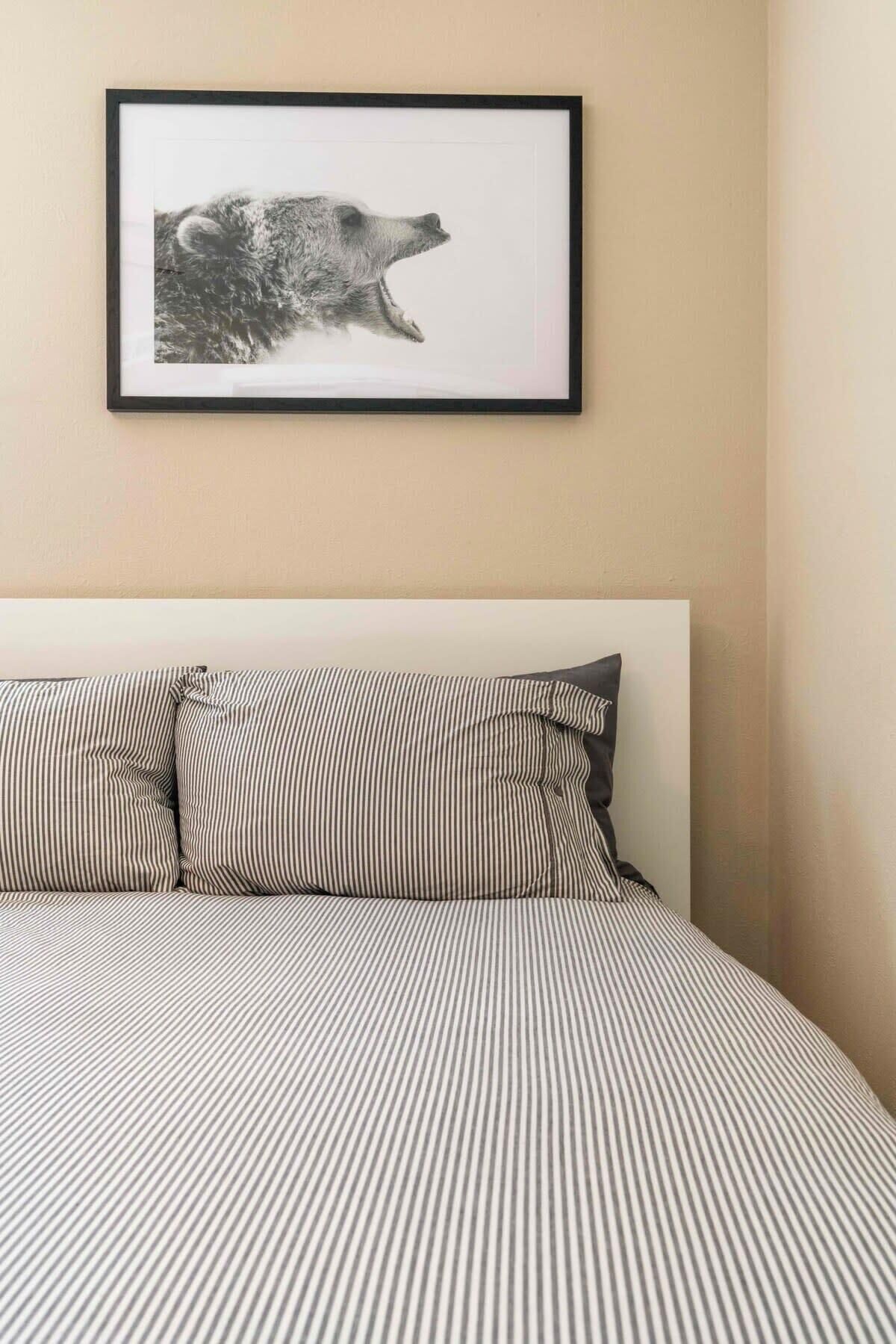 A bed with striped bedding and a framed picture of a bear on the wall.